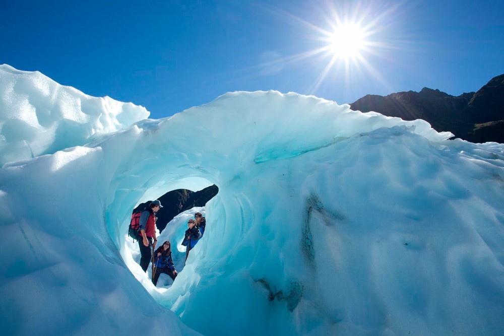 fotografía del glaciar en Nueva Zelanda con el cielo despejado y cuatro excursionistas 